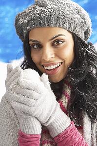 Young Woman Wearing Warm Winter Clothes And Hat Holding Snowball In Studio