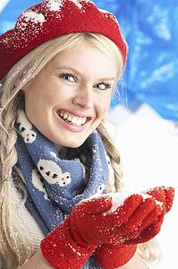 Young Woman Wearing Warm Winter Clothes And Hat Holding Snow In Studio