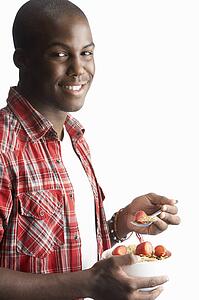 Young Man Eating Bowl Of Healthy Breakfast Cereal In Studio