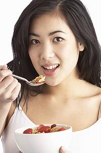 Young Woman Eating Bowl Of Healthy Breakfast Cereal In Studio