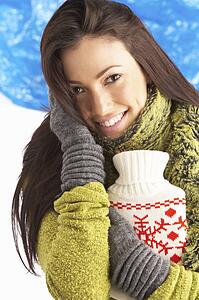 Young Woman Wearing Warm Winter Clothes Holding Hot Water Bottle In Studio
