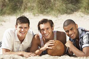 Three Young Men Relaxing On Beach With Football Together