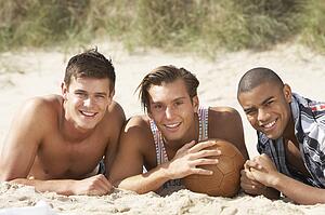 Three Young Men Relaxing On Beach With Football Together