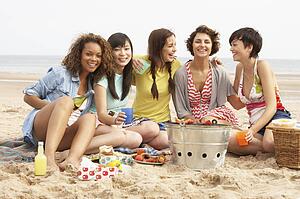 Group Of Girls Enjoying Barbeque On Beach Together