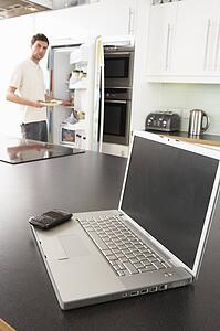 Young Man Fixing Snack In Kitchen With Laptop In Modern Kitchen 