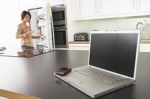 Young Woman Fixing Snack In Kitchen With Laptop In Modern Kitchen 