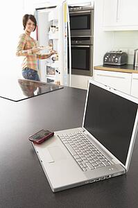 Young Woman Fixing Snack In Kitchen With Laptop In Modern Kitchen 