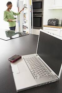 Young Woman Fixing Snack In Kitchen With Laptop In Modern Kitchen 