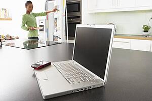 Young Woman Fixing Snack In Kitchen With Laptop In Modern Kitchen 