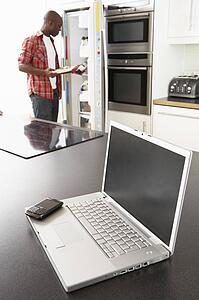 Young Man Fixing Snack In Kitchen With Laptop In Modern Kitchen 