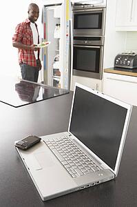 Young Man Fixing Snack In Kitchen With Laptop In Modern Kitchen 