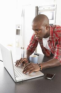 Young Man Using Laptop In Modern Kitchen 