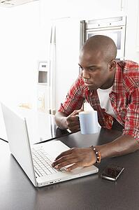 Young Man Using Laptop In Modern Kitchen 