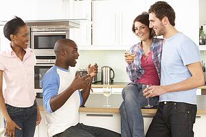 Group Of Young Friends Enjoying Glass Of Wine In Modern Kitchen
