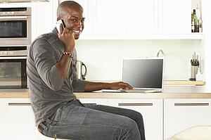 Young Man Relaxing Sitting In Kitchen Talking On Phone