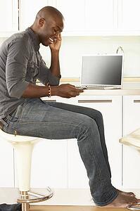 Young Man Relaxing Sitting In Kitchen Talking On Phone