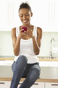 Woman Using Mobile Phone Sitting In Modern Kitchen 