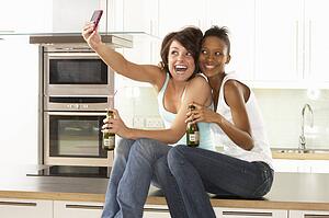 Two Girlfriends Taking Photo With Digital Camera In Modern Kitchen
