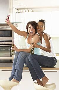 Two Girlfriends Taking Photo With Digital Camera In Modern Kitchen