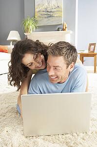 Couple Using Laptop Relaxing Laying On Rug At Home