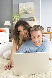 Couple Using Laptop Relaxing Laying On Rug At Home