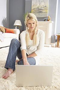 Woman Using Laptop To Manage Household Bills Laying On Rug At Home 