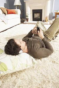 Man Listening To MP3 Player On Headphones Relaxing Laying On Rug At Home 