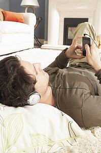 Man Listening To MP3 Player On Headphones Relaxing Laying On Rug At Home 