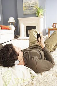 Man Listening To MP3 Player On Headphones Relaxing Laying On Rug At Home 