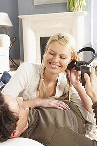 Couple Listening To MP3 Player On Headphones Relaxing Laying On Rug At Home 