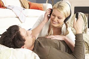 Couple Listening To MP3 Player On Headphones Relaxing Laying On Rug At Home 