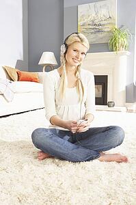 Woman Listening To MP3 Player On Headphones Relaxing Sitting On Rug At Home 