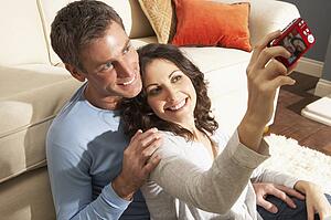 Couple Taking Photograph On Digital Camera At Home 