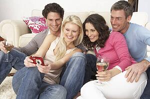 Group Of Friends Looking At Pictures On Digital Camera At Home
