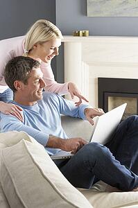 Couple Using Laptop Relaxing Sitting On Sofa At Home