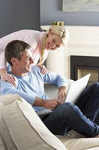 Couple Using Laptop Relaxing Sitting On Sofa At Home
