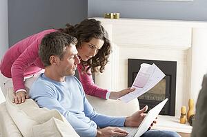 Couple Using Laptop And Discussing Household Bills Sitting On Sofa At Home
