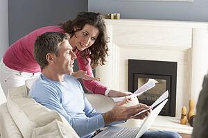 Couple Using Laptop And Discussing Household Bills Sitting On Sofa At Home