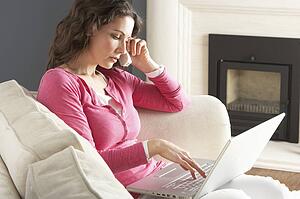 Woman Using Laptop Relaxing Sitting On Sofa At Home Talking On Phone