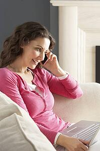 Woman Using Laptop Relaxing Sitting On Sofa At Home Talking On Phone