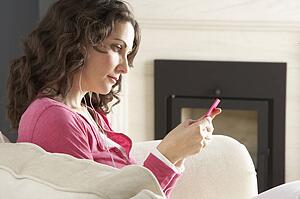 Woman Listening To MP3 Player On Headphones Relaxing Sitting On Rug At Home 