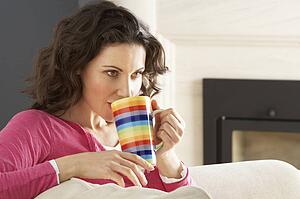 Woman Relaxing On Sofa At Home Drinking Cup Of Coffee