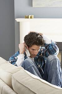 Stressed Man Sitting On Sofa At Home Talking On Phone