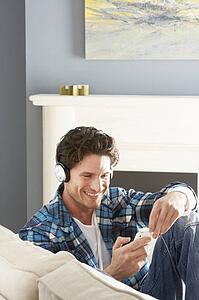 Man Listening To MP3 Player On Headphones Relaxing Sitting On Sofa At Home 