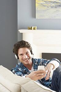 Man Listening To MP3 Player On Headphones Relaxing Sitting On Sofa At Home 