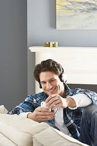 Man Listening To MP3 Player On Headphones Relaxing Sitting On Sofa At Home 