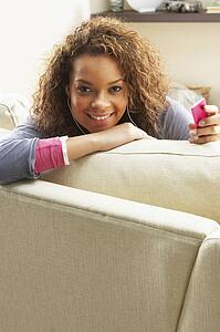 Woman Listening To MP3 Player On Headphones Relaxing Sitting On Rug At Home 