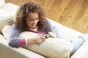 Woman Looking At Pictures On Digital Camera Relaxing Sitting On Sofa At Home