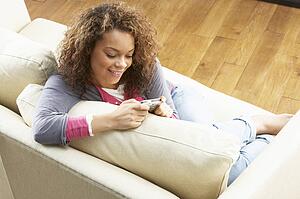 Woman Looking At Pictures On Digital Camera Relaxing Sitting On Sofa At Home