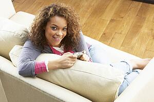 Woman Looking At Pictures On Digital Camera Relaxing Sitting On Sofa At Home 